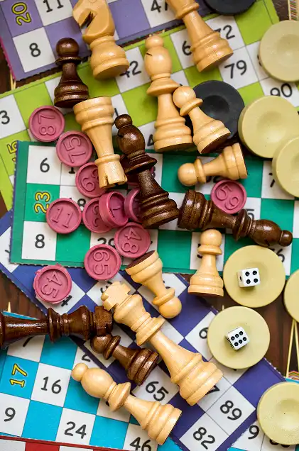 Wooden chess pieces, bingo chips, dice and classic board game elements scattered on colorful game boards on the table.