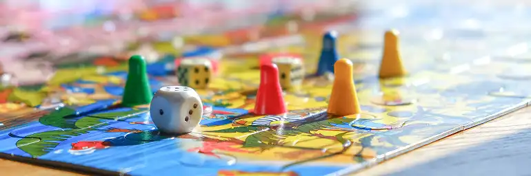 Close-up of colorful board game pieces and dice on a brightly colored board game board with shallow depth of field.